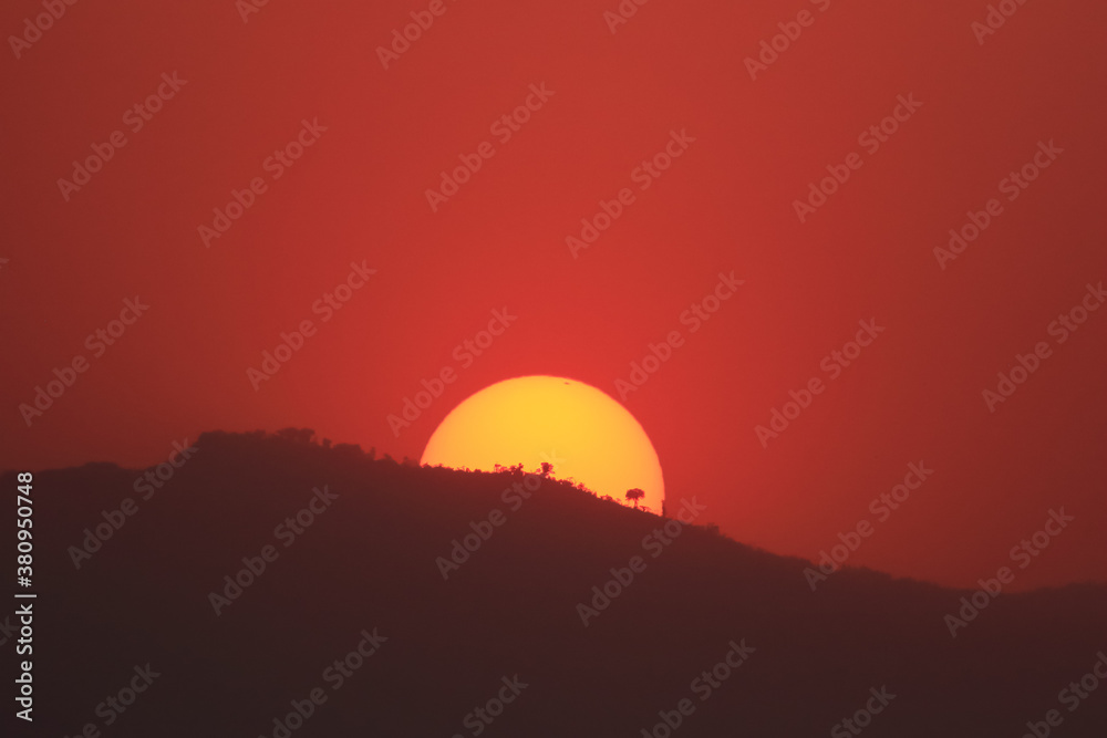Sun setting behind a hill with the sky turning red