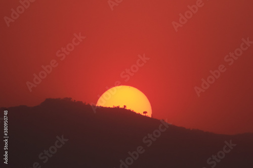 Sun setting behind a hill with the sky turning red
