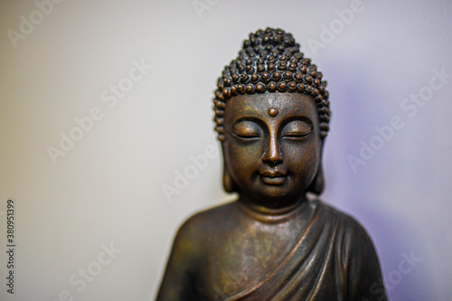 Peaceful bronze buddhist meditating Buddha head sculpture face sitting against simple white wall with shadow
