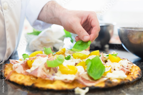 Italian cuisine: preparation of white pizza, with yellow tomatoes, white mozzarella, red ham and green basil. Design serving. professional cook at work. food photography for menus and websites