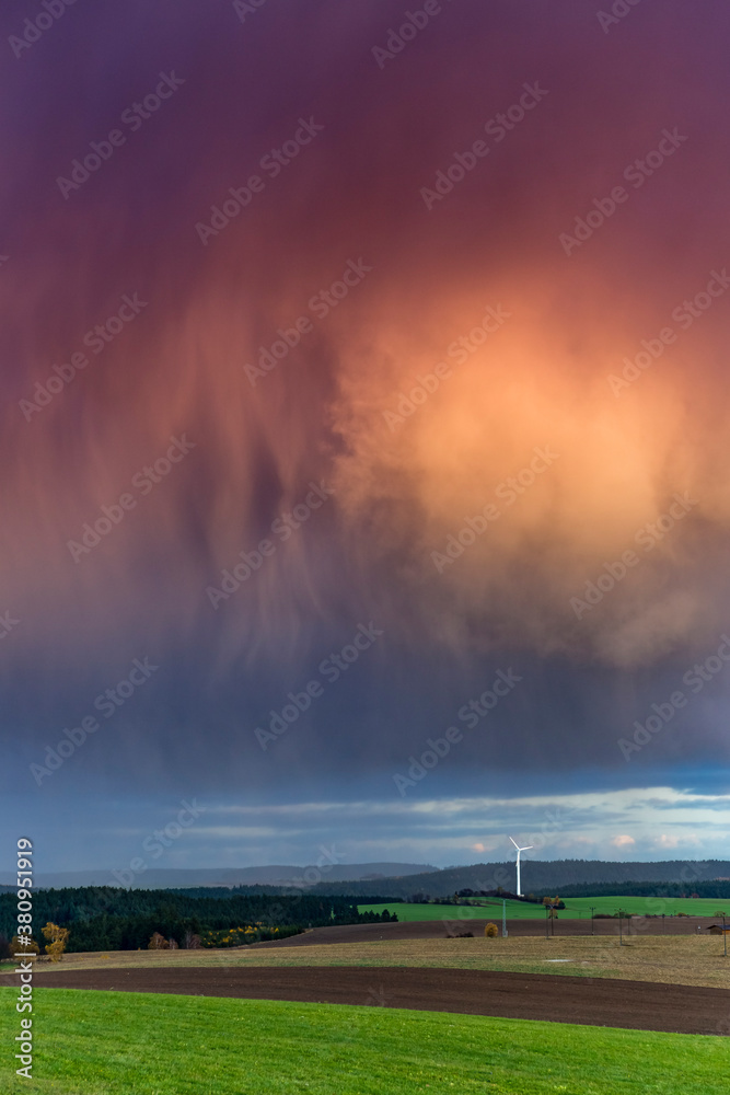 Thunderstorm is coming with rain, clouds are warm illuminated from the sun,on the horizont blue sky, Kulm, Thuringia, Germany