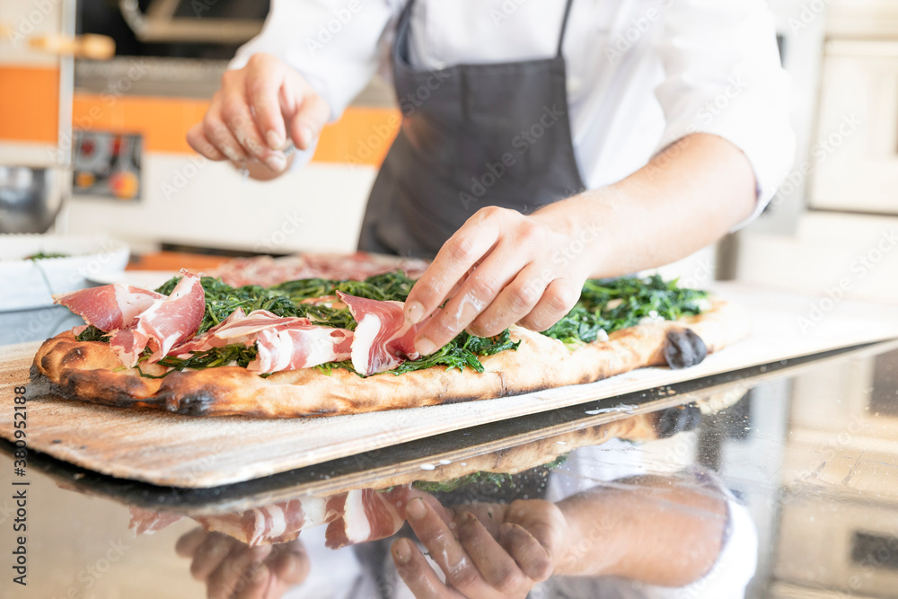 Italian cuisine: preparation of white pizza, with red ham, white mozzarella and green vegetables. Design serving. professional cook at work. food photography for menus and websites