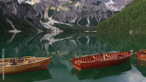 Revealing drone flight over floating wooden rowing boats and emerald green lake (Lago di Braies) towards beautiful moody mountain ranges in the Dolomites in Italy
