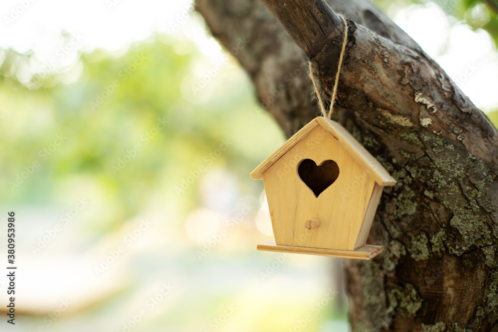 Wooden birdhouse hanging from tree in autumn garden. Concept for new home. A bird house or bird box in summer sunshine with natural green leaves background. Sweet home. Mini toy house. property