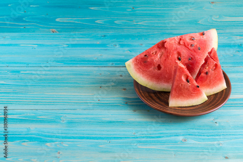 Three slices of ripe fresh watermelon lie in a clay plate on a blue wooden table
