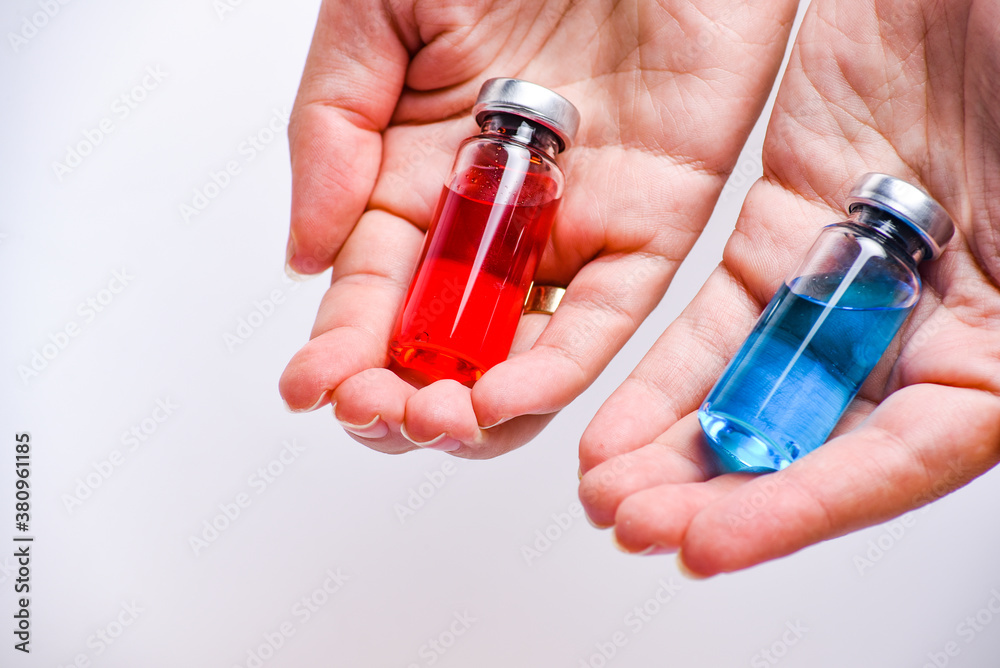 Concept of choice treatment. Close up Woman hands holding two vial or ampoules. Medical ampoules with liquid. Red and blue ampoules. Concept of choice treatment. Close up Woman hands holding two vial or ampoules. Medical ampoules with liquid. Red and blue ampoules.