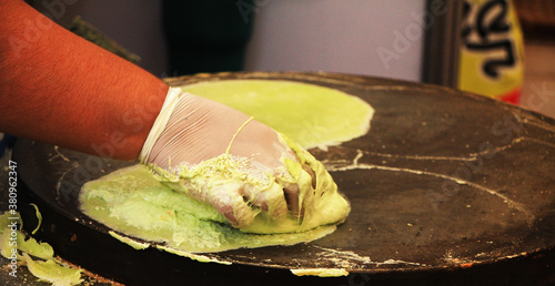 The hand man is making roti by applying the kneaded flour onto the pan and making a sheet for eating.