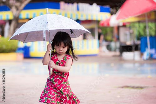 Foto Adorable little girl wearing a red dress with watermelon prints walks an umbrella on a drizzly day in the rainy season