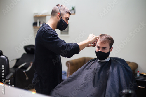 Man getting hair cut at the barber shop wearing protective mask during coronavirus pandemic
