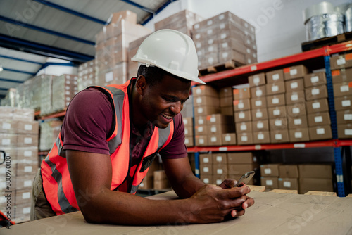 Mixed race male browsing on cellular device chatting to colleagues standing in warehouse