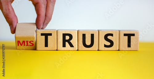 Hand turns a cube and changes the expression 'mistrust' to 'trust'. Beautiful yellow table, white background, copy space. Business concept.