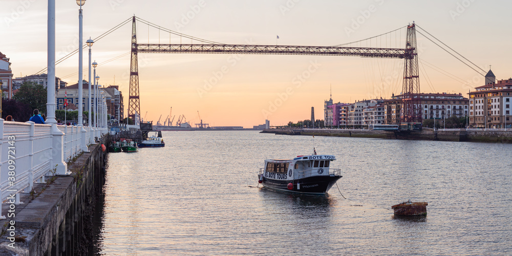 puente colgante de portugalete se ven edificios, mar y unos barcos pesqueros flotando 
