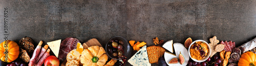 Fall charcuterie border against a dark stone banner background. Assorted cheese and meat appetizers. Copy space.