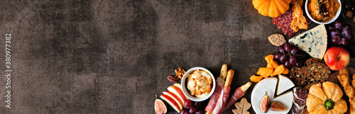 Autumn charcuterie corner border against a dark stone banner background. Selection of cheese and meat appetizers. Copy space.
