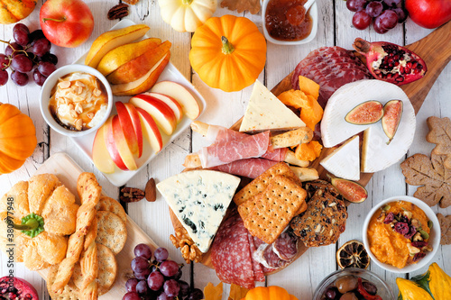 Fall theme charcuterie table scene against a white wood background. Assortment of cheese and meat appetizers. Above view.