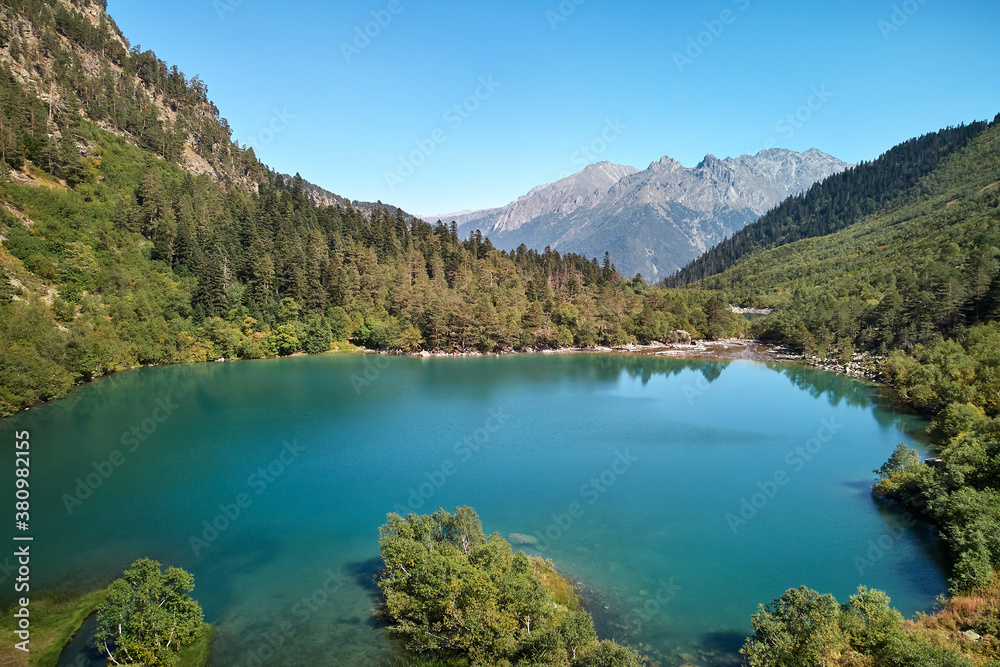 Blue water in a mountain forest lake with pine trees. Aerial view in the mountains on a blue lake and green forests. View on the lake between mountain forest. Fresh water