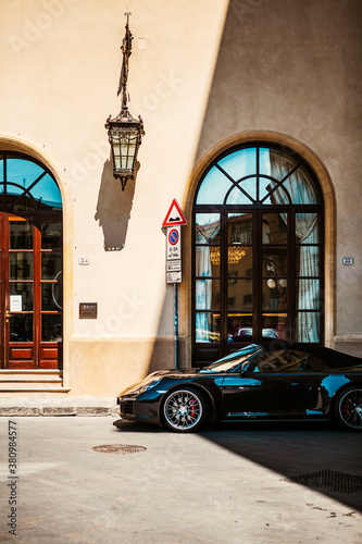 A black, fast, expensive car parked near the door and window of an Italian restaurant under a street lamp in the center of Florence, Tuscany, Italy. European style and trasportation