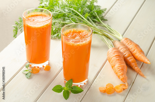 Freshly squeezed carrot juice in a glass on a wooden background with fresh carrots