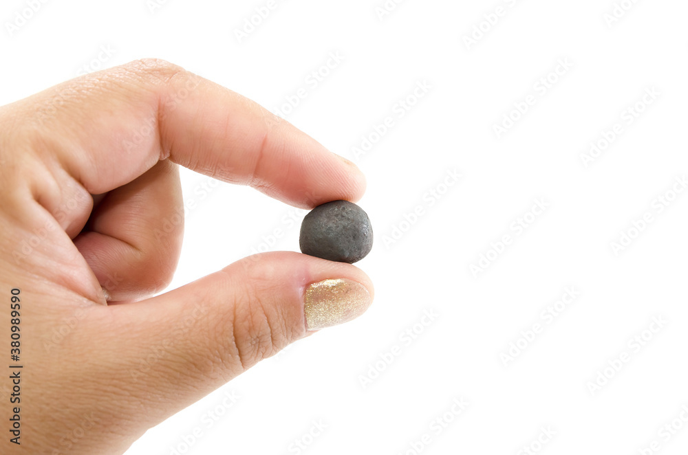 female hand holds with fingers a pellet of iron ore on a white background. female hand holds with fingers a pellet of iron ore on a white background.