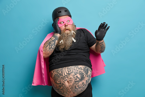 Frightened coward bearded man in superhero costume spends laisure time with kids playing cartoon characters sees something awful stares bugged eyes full of fear isolated on blue studio background photo