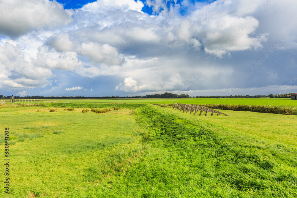 Fototapeta premium Landscape former Zuiderzee Island Schokland in the Dutch Noordoostpolder created by the drying of the IJsselmeer with wooden ice breakers against drift iceand sky with scattered clouds