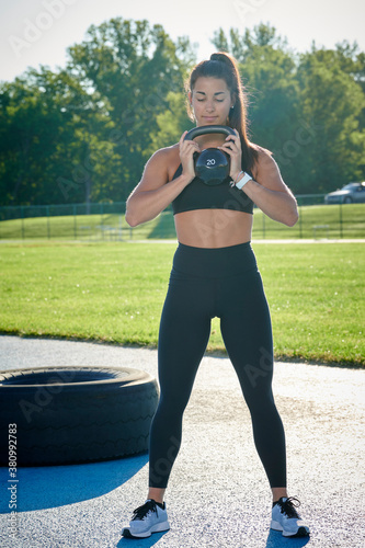 Beautiful young female works out at outdoor track - working our with kettle bell photo