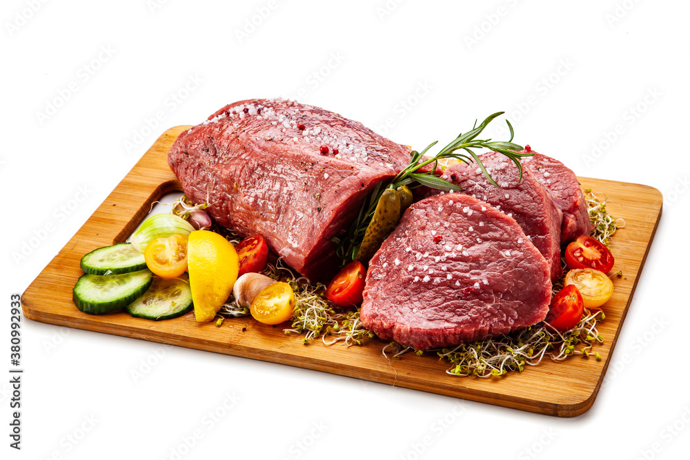 Fresh raw beef on cutting board with fresh vegetables on white background
