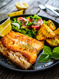 Fish dish - fried cod fillet with potatoes and vegetable salad on wooden table

