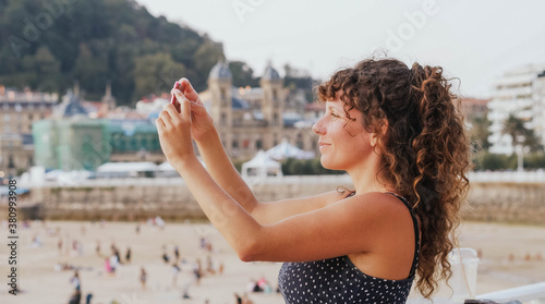 Curly-haired tourist woman takes photos with her smartphone in the city of San Sebastian, Spain. Cultural tourism 