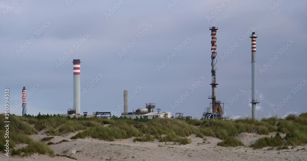 Several industrial chimneys rise among the dunes of a protected landscape, destruction of the atmosphere, ozone layer, the life of the planet