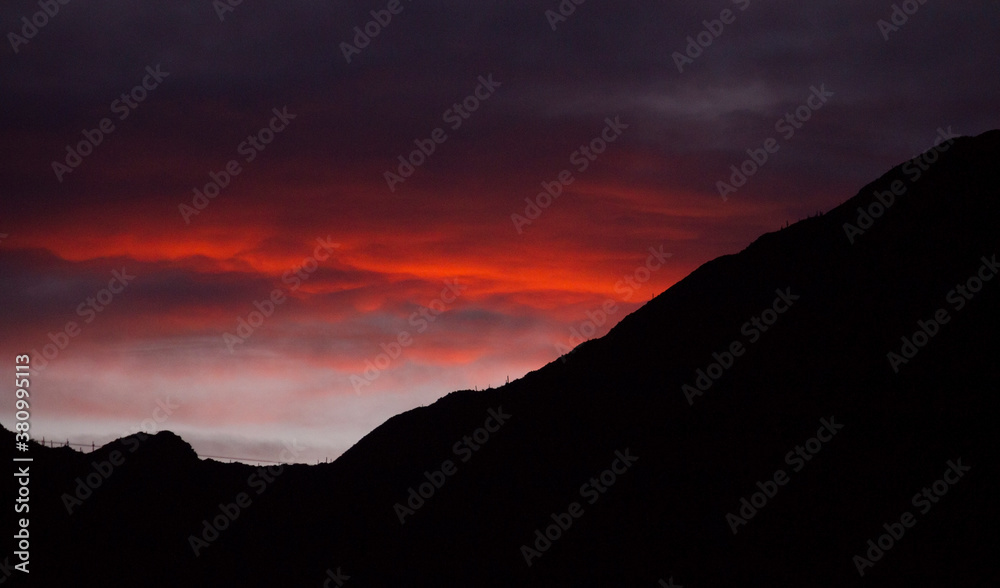 Dramatic sunset. View of the dark mountains silhouette and beautiful sky at twilight. Dusk red and orange colors in the clouds and sky.  