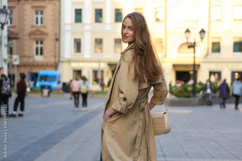 Fototapeta premium beautiful young woman posing on the street of old european city. girl model wearing trench coat outdoors. casual style lady model posing on urban background