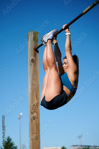 Beautiful young female works out at outdoor track - in teal sports bra and shorts - doing pull ups