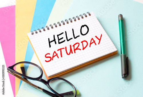The Notepad with the text Hello Saturday is on colored paper with glasses and a pen