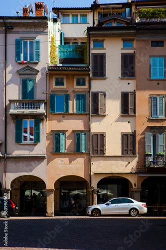 Close up. The facade of the vintage Italian buildings with arches, columns, wooden shutters, tiled roofs and the cars nearby in the city center of Bergamo, Lombardy, Italy. Old European architecture © Andrei_Molchan