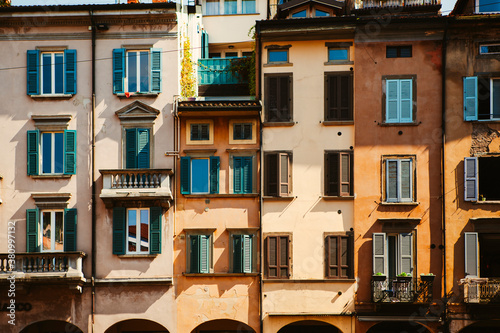 Fototapeta Naklejka Na Ścianę i Meble -  Close up. The facade of the vintage Italian buildings with arches, columns, wooden shutters, tiled roofs and the cars nearby in the city center of Bergamo, Lombardy, Italy. Old European architecture
