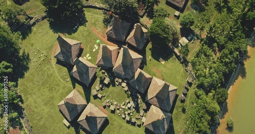 Top down of traditional Indonesia houses aerial view. Unique countryside cottages on green grass valley at ocean bay of Waikabubak, Kampung Tarung, Sumba Island. Summer nature landscape drone shot photo