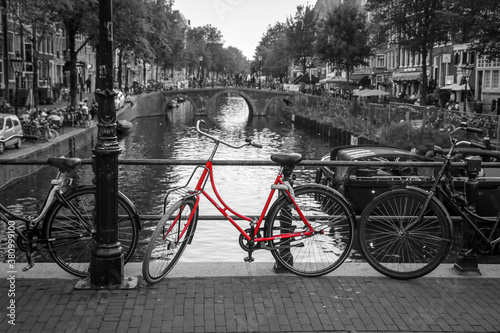 A picture of a red bike on the bridge over the channel in Amsterdam. The background is black and white. © shootingtheworld