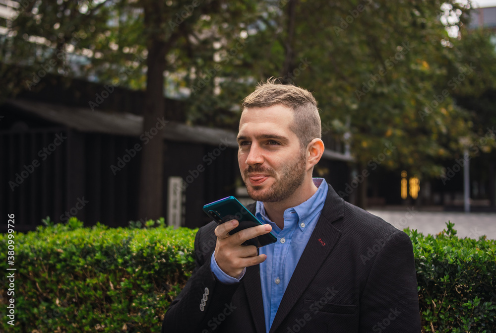 Photo of a young and attractive business man wearing smart casual clothes sending and audio with is phone in a job break Photo of a young and attractive business man wearing smart casual clothes sending and audio with is phone in a job break