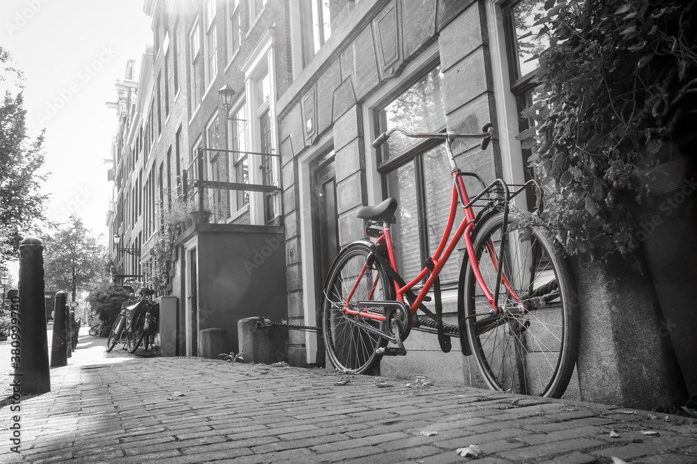Fototapeta Zdjęcie samotnego czerwonego roweru na ulicy przy kanale w Amsterdamie. Tło jest czarno-białe.