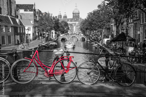 A picture of a red bike on the bridge over the channel in Amsterdam. The background is black and white. © shootingtheworld
