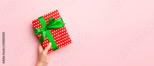 Female's hands holding striped gift box with colored ribbon on living coral background. Christmas concept or other holiday handmade present box, concept top view with copy space