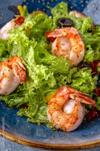 A light, nutritious salad of shrimp, lettuce and olives. Natural delicious food. Greek cuisine menu. Still life in a marine style on a blue background.