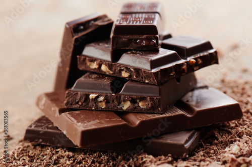 Composition of bars and pieces of different milk and dark chocolate, grated cocoa on a brown background side view close up