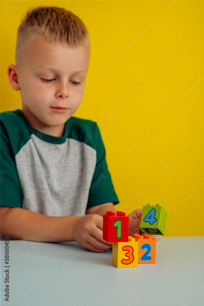 The child playing with cubes with numbers on the table.On a yellow background.Concept of early child development The child playing with cubes with numbers on the table.On a yellow background.Concept of early child development