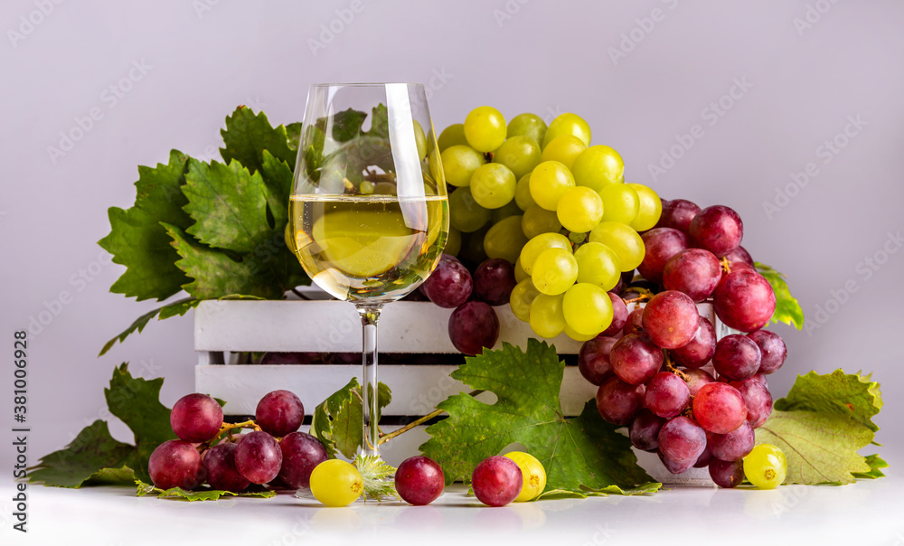 Glass with white sparkling wine, green and pink grapes with leaves in a white box
