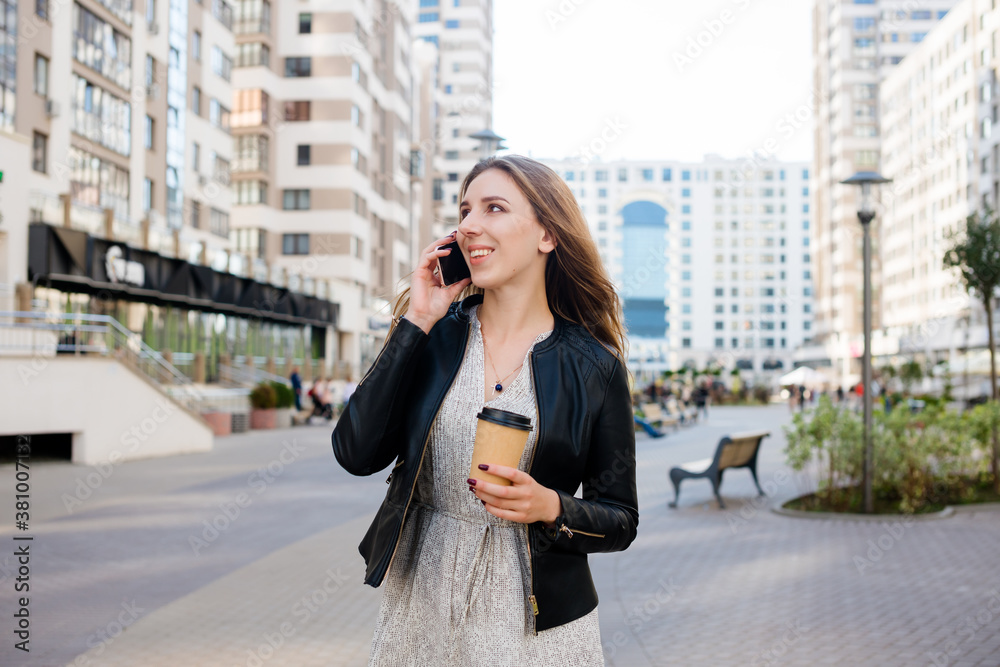 Beautiful woman is speaking on the phone with a cup of coffee at the city street background. Beautiful woman is speaking on the phone with a cup of coffee at the city street background.
