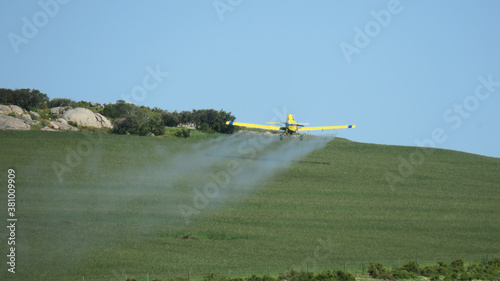 Crop duster spraying fertliizer over green cropse
