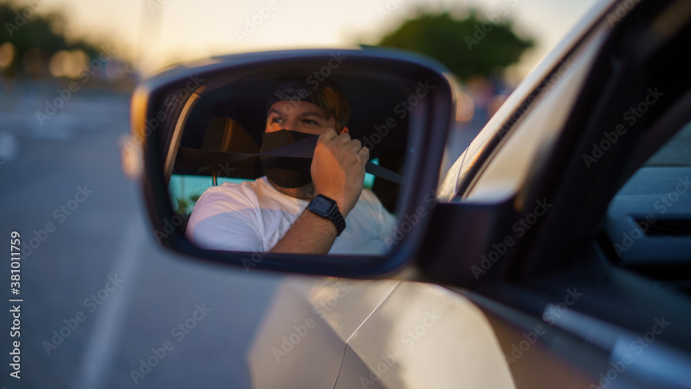 Chico joven conduciendo su coche recien lavado y comprobando los espejos y cinturones usando mascarilla de la pandemia de coronavirus covid-19