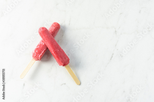 Two bright red icy popsicles crossed on top of each other with copy space on white and gray marble